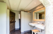Baño moderno en tienda safari con dos lavabos, espejo grande y detalles rústicos de madera junto a la granja.