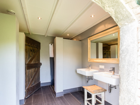 Baño moderno en tienda safari con dos lavabos, espejo grande y detalles rústicos de madera junto a la granja.