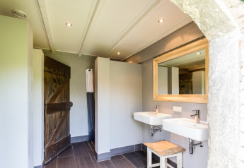 Baño moderno en tienda safari con dos lavabos, espejo grande y detalles rústicos de madera junto a la granja.