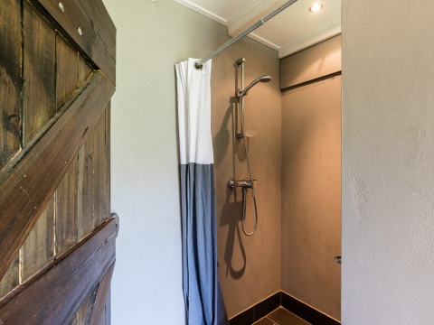 Privé hete douche in een safaritent met houten schuurdeur en douchegordijn bij de boerderij.