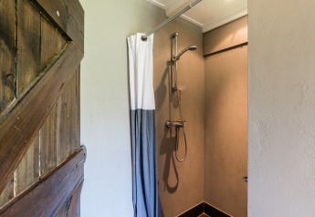 Douche privée avec eau chaude dans une tente safari, rideau et porte rustique chez l’agriculteur.