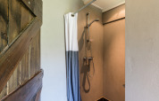 Private hot shower at the farmer's house inside a safari tent, featuring a modern shower and rustic door.