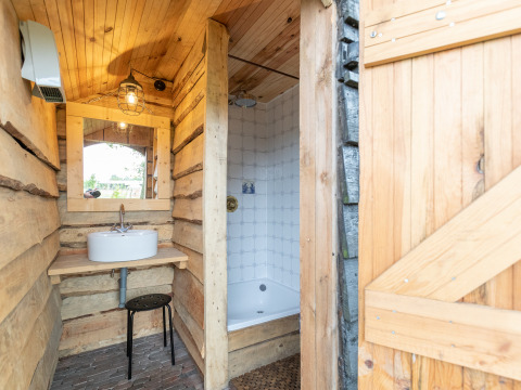 Baño rústico en tienda safari con paredes de madera, lavabo, espejo y ducha privada en la casa del granjero.