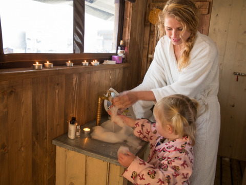 Mother and child wash hands in a safari tent cottage with candles, wood walls and private shower.