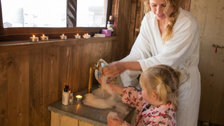 Mère et enfant se lavent les mains dans une tente safari boisée, bougies allumées et douche privée.