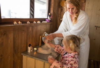 Moeder en kind wassen hun handen in een safaritent met houten wanden, kaarsen en privé-douche.