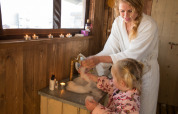 Mother and child wash hands in a safari tent cottage with candles, wood walls and private shower.