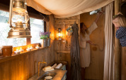 Interior view of a safari tent cottage with private hot shower, candles, lanterns, and two women inside.