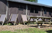 Área de descanso al aire libre con sillas y mesa frente a una casa-tienda safari con ducha privada en la granja.