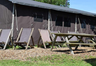 Liegestühle und Picknicktisch vor einem Safari-Zelt mit privater Dusche auf dem Bauernhof.
