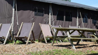Outdoor seating area with deck chairs and picnic table in front of safari tent house with private shower.