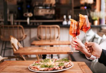 Deux personnes trinquent avec des cocktails devant une pizza sur une table en bois dans un restaurant glamping.