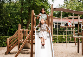 Due bambini giocano sul parco giochi di una sistemazione glamping, uno scivola giù dallo scivolo.