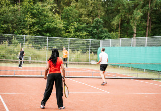 Quattro persone giocano a tennis su un campo all’aperto circondato da alberi in una sistemazione glamping.