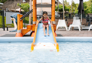 Petite fille en maillot de bain descendant un toboggan dans une piscine sur un site de glamping extérieur.