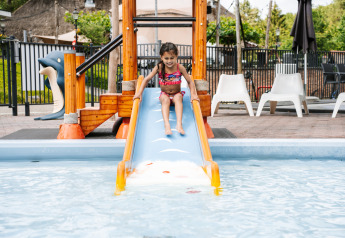Bambina in costume da bagno scivola su uno scivolo d'acqua in piscina in un'area glamping all'aperto.