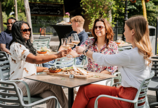 Tres mujeres brindan con copas de vino en una mesa exterior de glamping, rodeadas de comida y naturaleza.