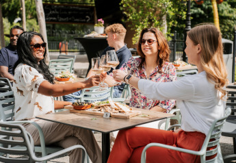 Drei Frauen stoßen mit Weingläsern an einem Tisch im Freien auf einem Glampingplatz an, umgeben von Essen.