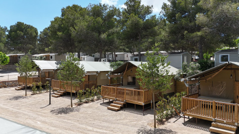 Safari tents named Outback at Vilanova Park Campsite in Spain with wooden decks, surrounded by green trees.