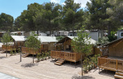 Safari-telte ved Vilanova Park Campingplads i Spanien, omgivet af træer og med træterrasser foran.