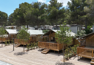 Outback safari-tenten op Vilanova Park Camping in Spanje met houten terrassen en omgeven door bomen.