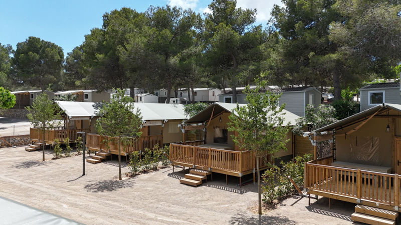 Tiendas safari Outback en el camping Vilanova Park en España, rodeadas de árboles y terrazas de madera.