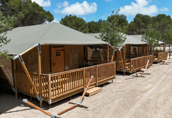 Tentes safari avec vérandas en bois au camping Vilanova Park en Espagne sous un ciel lumineux.