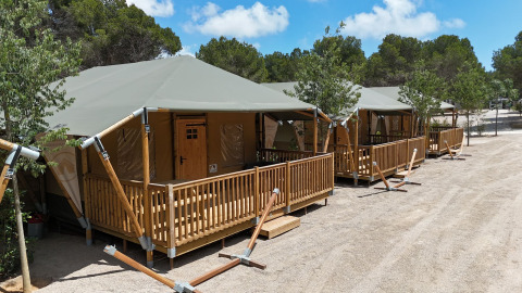 Tiendas safari con porches de madera en el camping Vilanova Park en España bajo un cielo soleado.