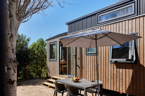 Zona de comedor exterior con mesa y sombrilla en Tiny Home Arrozal, TAIGA Delta de l'Ebre, España.