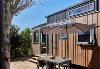 Udendørs spiseplads med parasol ved det lille hus Tiny Home Arrozal ved TAIGA Delta de l'Ebre i Spanien.