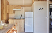 Kleine, moderne Küche im Tiny Home Arrozal bei TAIGA Delta de l'Ebre, Spanien, mit Holzfronten und weißem Kühlschrank.