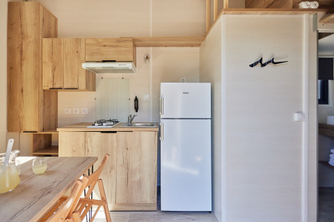 Moderne og kompakt køkken i Tiny Home Arrozal på TAIGA Delta de l'Ebre, Spanien, med træskabe og hvidt køleskab.