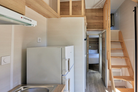 Interiør af et lille hus med køkken, trappe til hems og synligt soveværelse i Tiny Home Arrozal, Spanien.
