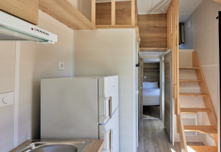 Interiør af et lille hus med køkken, trappe til hems og synligt soveværelse i Tiny Home Arrozal, Spanien.