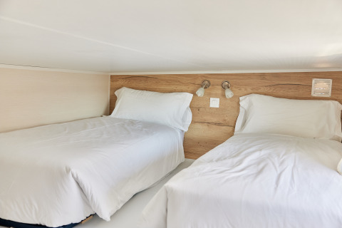 Two single beds with white linens in a cozy loft of Tiny Home Arrozal at TAIGA Delta de l'Ebre, Spain.