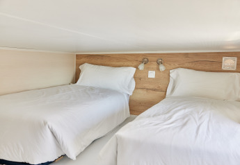 Deux lits simples avec draps blancs dans une mezzanine cosy de Tiny Home Arrozal à TAIGA Delta de l'Ebre, Espagne.