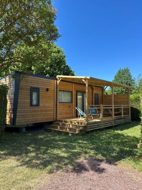 Cabaña Prestige Cottage en Camping Seasonova Les Marguerites, Francia, rodeada de césped y cielo azul.