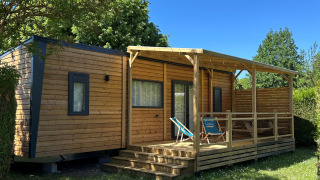 Cabaña Prestige Cottage en Camping Seasonova Les Marguerites, Francia, rodeada de césped y cielo azul.