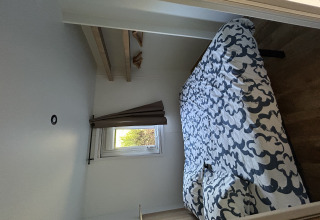 Pequeño dormitorio con cama doble, ventana y estantes en Prestige Cottage, Camping Seasonova Les Marguerites.