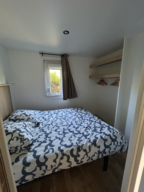 Pequeño dormitorio con cama doble, ventana y estantes en Prestige Cottage, Camping Seasonova Les Marguerites.