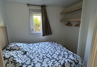 Lille soveværelse med dobbeltseng, vindue og hylder på Prestige Cottage, Camping Seasonova Les Marguerites.