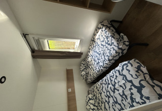 Værelse med to enkeltsenge, moderne mønstrede dynebetræk, vindue og trægulv i Prestige Cottage, Camping Seasonova Les Marguerites, Frankrig.