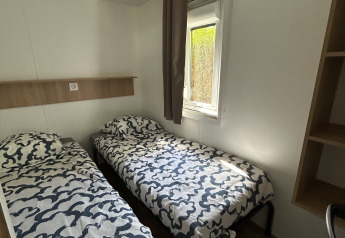 Værelse med to enkeltsenge, moderne mønstrede dynebetræk, vindue og trægulv i Prestige Cottage, Camping Seasonova Les Marguerites, Frankrig.