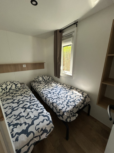 Chambre avec deux lits simples, draps à motifs modernes, fenêtre et sol en bois au Prestige Cottage du Camping Seasonova Les Marguerites, France.