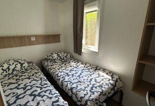 Chambre avec deux lits simples, draps à motifs modernes, fenêtre et sol en bois au Prestige Cottage du Camping Seasonova Les Marguerites, France.