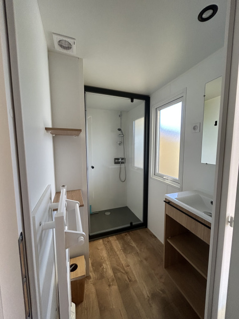 Baño moderno en Prestige Cottage, Camping Seasonova Les Marguerites, Francia, con ducha, lavabo y suelo de madera.