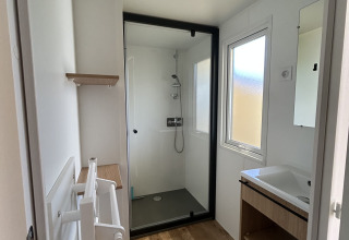 Bagno moderno nel Prestige Cottage al Camping Seasonova Les Marguerites, Francia, con doccia, lavandino e pavimento in legno.