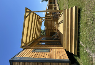 Cabaña de madera con terraza y sillas en Camping Seasonova Les Marguerites en Francia bajo cielo azul.
