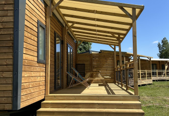 Houten huisje met terras en stoelen op Camping Seasonova Les Marguerites in Frankrijk onder blauwe lucht.