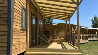 Holzhütte mit Veranda und Stühlen auf Camping Seasonova Les Marguerites in Frankreich bei Sonnenschein.